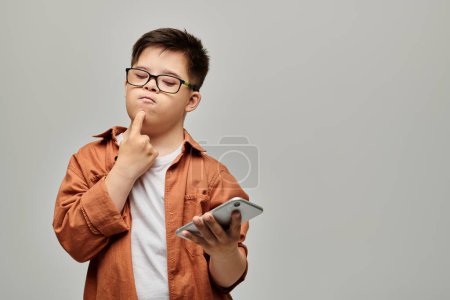 Téléchargez les photos : Petit garçon avec le syndrome de Down tenant un téléphone portable, regardant absorbé. - en image libre de droit