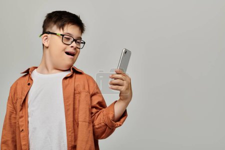 Foto de Un niño con síndrome de Down con gafas sostiene un teléfono celular. - Imagen libre de derechos
