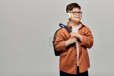 Ein kleiner Junge mit Down-Syndrom trägt Kopfhörer und einen Rucksack.