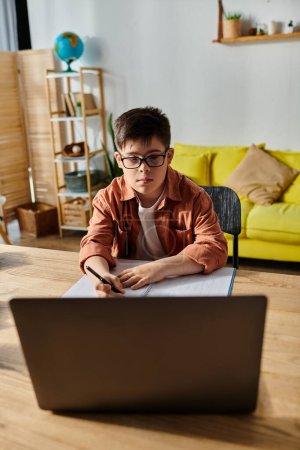 A boy with Down syndrome sitting at table, using laptop.