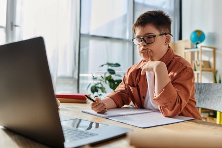 Kleiner Junge mit Down-Syndrom mit Brille studiert am Schreibtisch am Laptop.