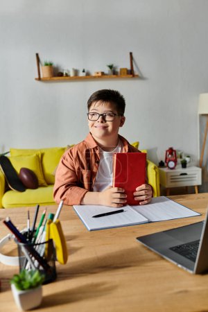 A boy with Down syndrome sitting at a desk, using a laptop and notebook.