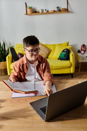 A boy with Down syndrome sitting at a table with a laptop and a book.