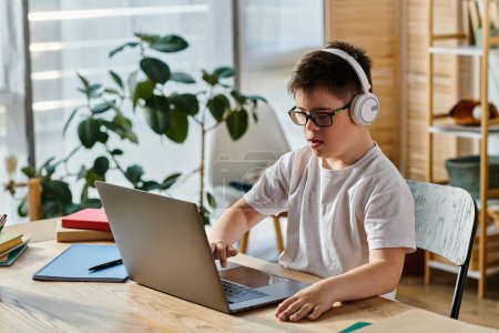 Photo for A boy with Down syndrome uses a laptop at home while wearing headphones. - Royalty Free Image