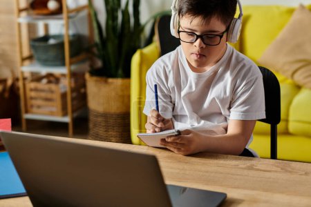 A adorable boy with Down syndrome is engrossed in using a laptop and wearing headphones at a table.
