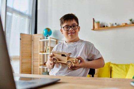 Foto de Adorable boy with Down syndrome playing with a wooden toy car in front of a laptop. - Imagen libre de derechos