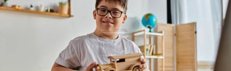 Un niño con síndrome de Down con gafas juega con un coche de juguete de madera.