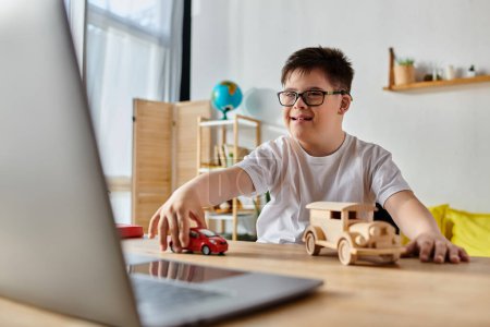 Kleiner Junge mit Down-Syndrom spielt mit Spielzeugauto auf Laptop in seinem Zimmer.