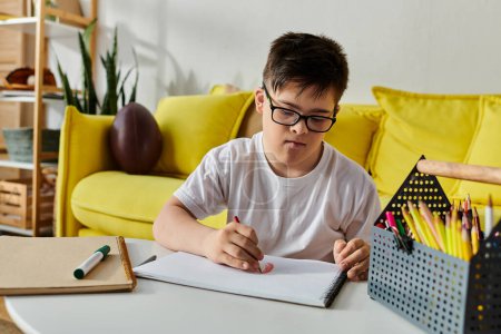 Foto de Un niño con síndrome de Down sentado en una mesa, centrado en escribir en un cuaderno. - Imagen libre de derechos