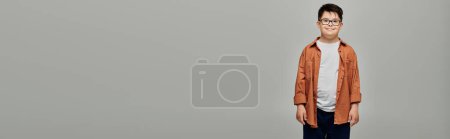 Téléchargez les photos : Un petit garçon trisomique se dresse sur un fond gris. - en image libre de droit