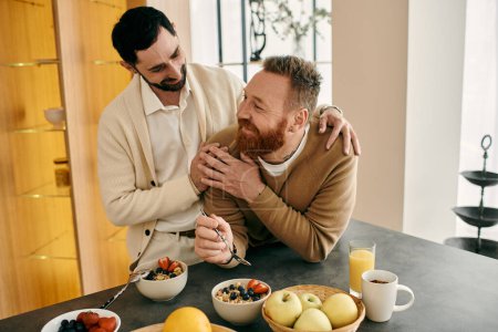 Two men, a happy gay couple, are hugging each other warmly in their modern apartment kitchen.
