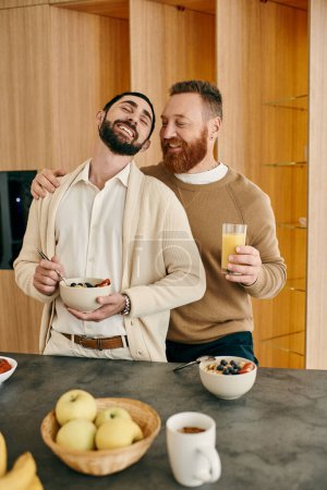 Happy gay couple stands in modern kitchen, sharing a bowl of fresh fruit. Quality time and love is evident in their smiles.
