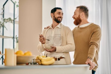Zwei glückliche bärtige Männer, ein schwules Paar, das zusammen in einer modernen Küche steht und einen Moment der Verbundenheit und Zeit genießt.