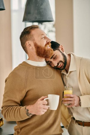 A happy gay couple embraces while enjoying a cup of coffee in their modern kitchen.