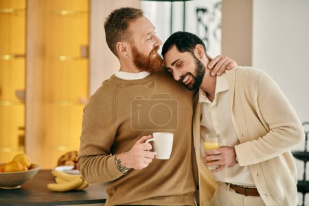 Two men, a happy gay couple, hug affectionately while savoring coffee in a modern kitchen, showcasing their love and connection.
