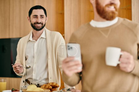 Foto de Una feliz pareja gay se encuentra en una cocina, sosteniendo el café mientras pasan tiempo de calidad juntos en su apartamento moderno. - Imagen libre de derechos