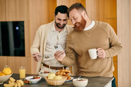 Foto de Dos hombres disfrutan del desayuno en una cocina elegante, absorbida en el teléfono mientras comparten momentos íntimos. - Imagen libre de derechos