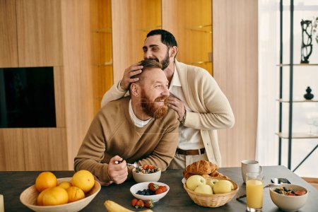 Two men, a happy gay couple, are sitting at a table in a modern apartment, enjoying breakfast together.