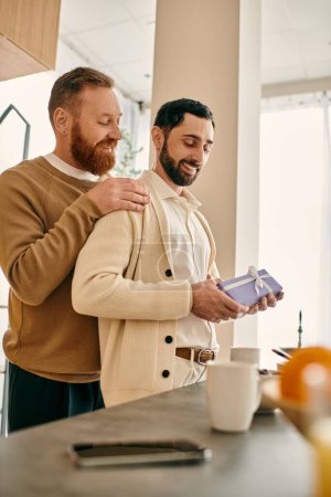 Couple gay heureux dans une cuisine appartement moderne, tenant un cadeau réfléchi l'un pour l'autre.