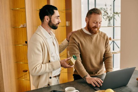 Téléchargez les photos : Deux hommes, un couple gay heureux, absorbé dans leur ordinateur portable dans une cuisine moderne, profiter de temps de qualité ensemble. - en image libre de droit