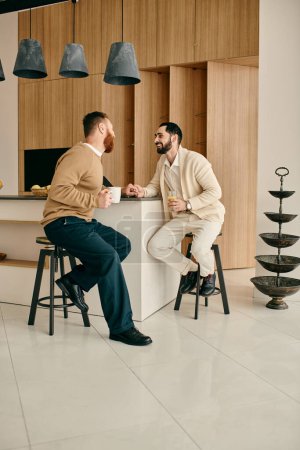 A happy gay couple sitting on stools in a modern kitchen, enjoying each others company and spending quality time together.