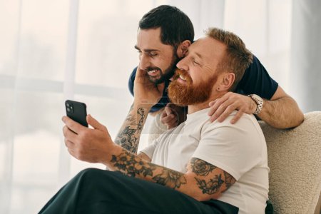 Two men in casual attire sitting on a couch, fully engaged with a cell phone.