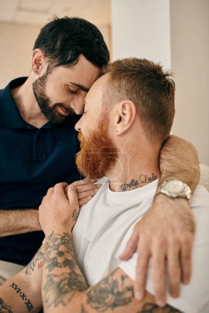 Two men with tattoos on their arms hug each other in a display of love and unity in a modern living room.