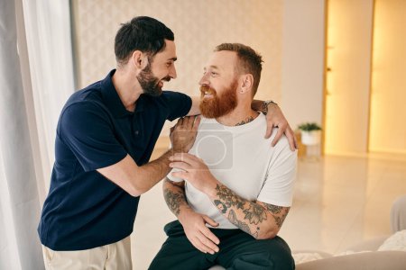 Two men in casual clothes hug each other warmly in a modern living room, showing affection and love in an intimate moment.