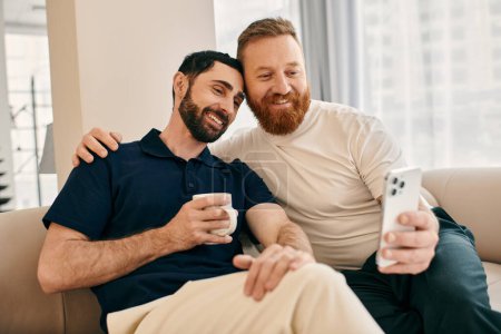 Foto de Dos hombres gay felices con ropa casual se sientan en un sofá, absortos en su teléfono celular, compartiendo un momento de conexión moderna. - Imagen libre de derechos