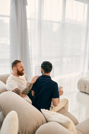 Dos hombres, una feliz pareja gay, relajarse en un moderno sofá de la sala de estar, envuelto en el amor y la conversación.