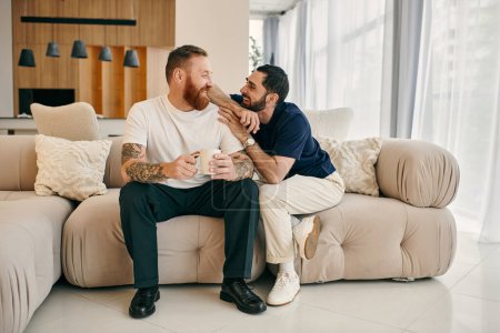 Téléchargez les photos : A happy gay couple in casual clothing sit closely together on a couch in a modern living room, enjoying quality time together. - en image libre de droit