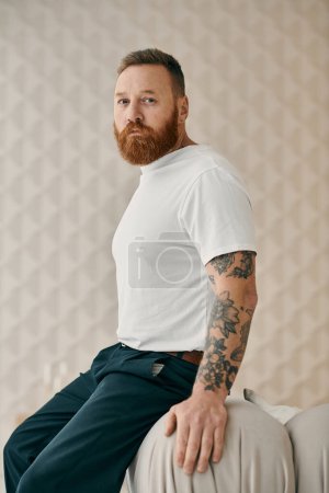 Ein Mann mit Bart sitzt gemütlich und gedankenverloren in einem modernen Wohnzimmer.