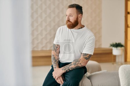 Téléchargez les photos : A man with a beard, sits comfortably on a couch in a modern living room. - en image libre de droit