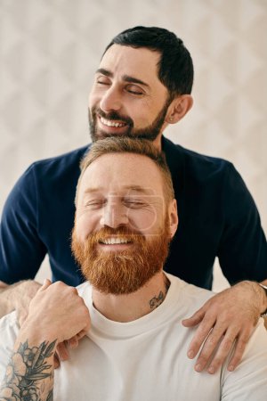 Foto de A happy gay couple, one with a red beard, sharing a warm hug in a cozy modern living room. - Imagen libre de derechos