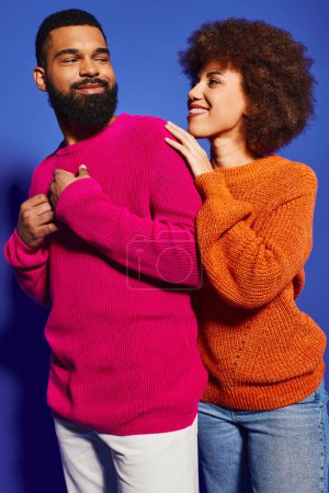 Téléchargez les photos : Les jeunes amis afro-américains, un homme et une femme, se tiennent ensemble dans une tenue décontractée dynamique sur un fond bleu. - en image libre de droit
