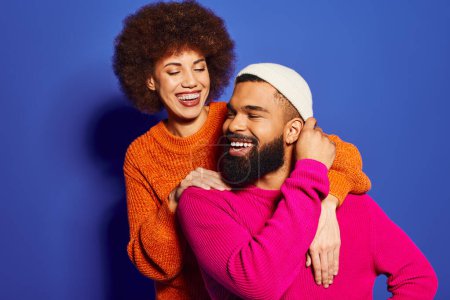 Foto de Un hombre barbudo y una mujer en trajes casuales coloridos comparten un cálido abrazo, que simboliza la amistad y la conexión. - Imagen libre de derechos