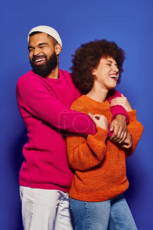 Photo for Young African American friends embrace warmly in vibrant attire, showcasing a beautiful bond of friendship on a blue background. - Royalty Free Image