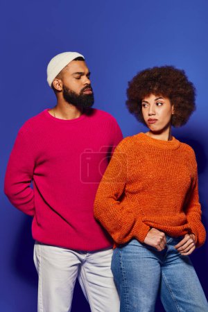 Un homme et une femme, amis en tenue décontractée vibrante, se tiennent ensemble en harmonie sur un fond bleu.