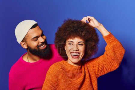 Foto de Un hombre y una mujer afroamericanos jóvenes, ambos con pelo afro, vestidos con un atuendo vibrante, exudando alegría y amistad sobre un fondo azul. - Imagen libre de derechos