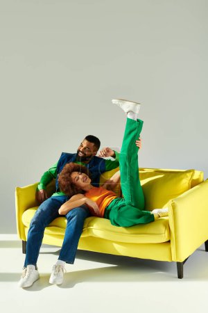 Photo for An African American man and woman, dressed in colorful attire, sit happily together on a bright yellow couch. - Royalty Free Image