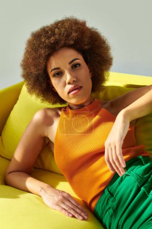 A woman of African descent sits peacefully atop a vibrant yellow couch