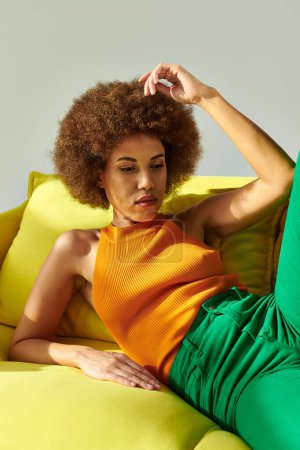 An African American woman in vibrant clothes sits on a yellow couch