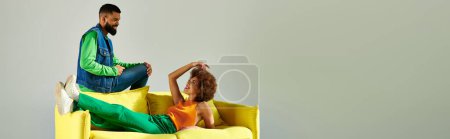 Photo for Happy African American friends in vibrant clothes sitting on a yellow couch against a grey background. - Royalty Free Image