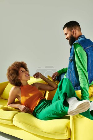 Foto de Un hombre y una mujer, amigos, sentados en un sofá amarillo, exudando felicidad y cercanía en su traje vibrante. - Imagen libre de derechos