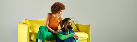 Téléchargez les photos : Heureux amis afro-américains en vêtements vibrants assis sur une chaise jaune sur un fond gris. - en image libre de droit