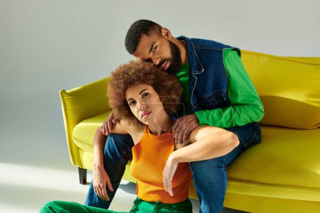 Un hombre y una mujer afroamericanos, vestidos vibrantemente, comparten un momento de amistad mientras están sentados en un sofá amarillo.