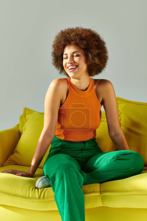 Téléchargez les photos : Une Afro-Américaine en vêtements vibrants est assise sur un canapé jaune - en image libre de droit