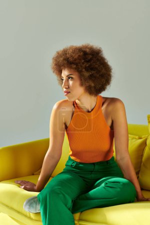 Téléchargez les photos : Une femme afro-américaine s'assoit gracieusement sur un canapé jaune, incarnant sérénité et dynamisme dans son environnement. - en image libre de droit