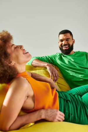 A man and a woman, happy African American friends, reclining on a bean bag chair in vibrant clothes, symbolizing friendship.