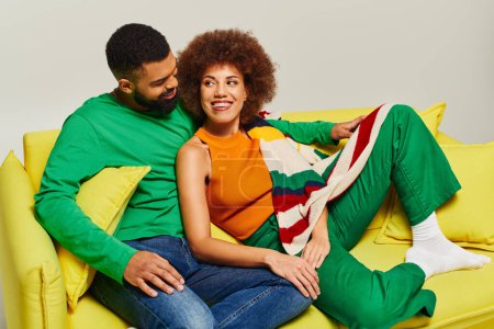 Téléchargez les photos : Heureux amis afro-américains en vêtements vibrants assis sur un canapé jaune, mettant en valeur le lien d'amitié entre un homme et une femme. - en image libre de droit